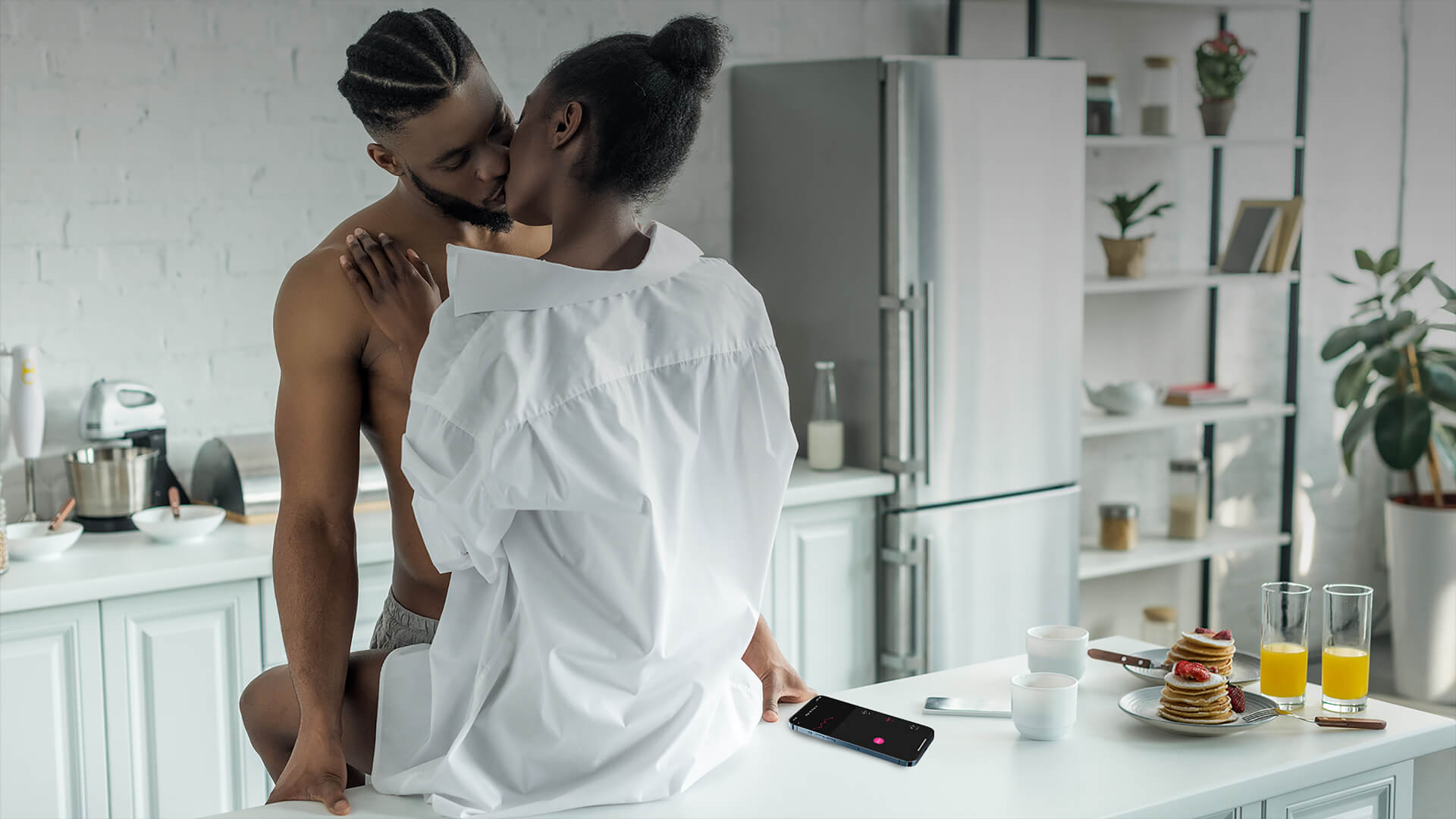 Lovense Ferri - Vorspiel in der Küche - ein nackter schwarzer Mann, der mit einer schwarzen Frau im weißen Hemd rummacht, während seine linke Hand ihren Ferri über die Lovense Remote App steuert