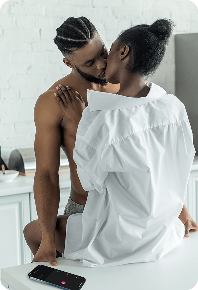 lovense ferri - foreplay in the kitchen- a naked black man making out with a black women in white shirt with his left hand controlling her ferri on the lovense remote app